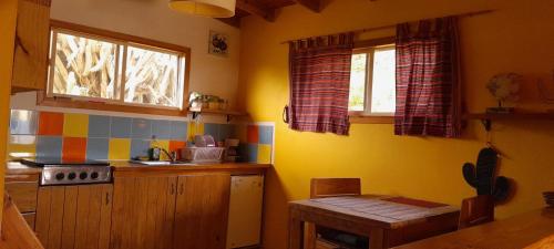 uma cozinha com paredes amarelas, uma mesa e janelas em Hopi Cadushi Apartment em Santa Cruz