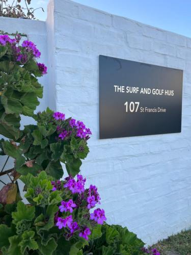 un cartello sul lato di un edificio con fiori viola di THE SURF AND GOLF HUIS Solar Power a St Francis Bay