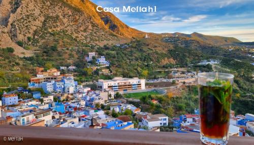 a glass of beer sitting on a balcony overlooking a city at Casa Meftah Blue in Chefchaouene