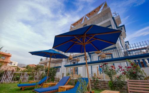 BLUE WAVE LODGE في Agadir nʼ Aït Sa: مجموعة من الكراسي الزرقاء والمظلات أمام المبنى