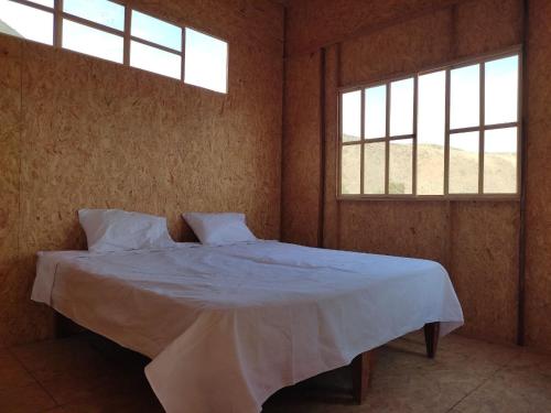 um quarto com uma cama com lençóis brancos e 2 janelas em Ese Lugar Retirado em Miraflores
