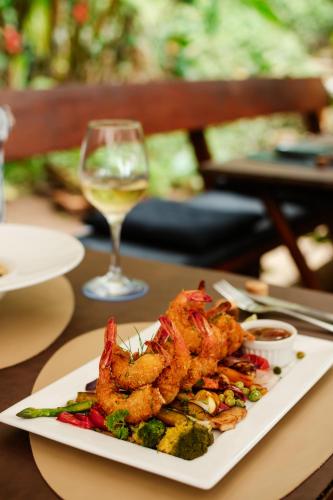 a plate of shrimp and vegetables with a glass of wine at Bonito Paraiso Ilha Grande in Abraão