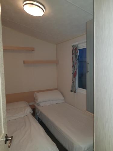 um pequeno quarto com 2 camas e uma janela em Beautiful 3-Bedrooms Static Caravan Holiday Home em Clacton-on-Sea
