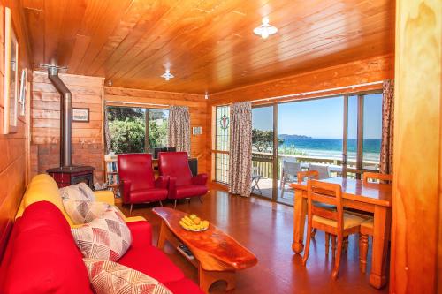 a living room with a red couch and a table at Sandy Bay Beachfront in Matapouri