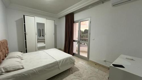 a white bedroom with a bed and a large window at Appartement Slim centre sousse in Sousse