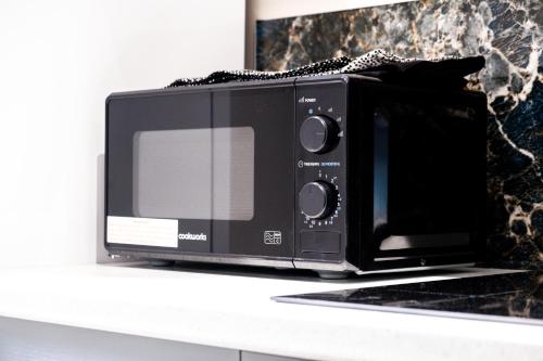 a black microwave sitting on top of a counter at MK 2-Bedroom Contractor's Gem, 5 beds, sleeps 6, free parking in Milton Keynes
