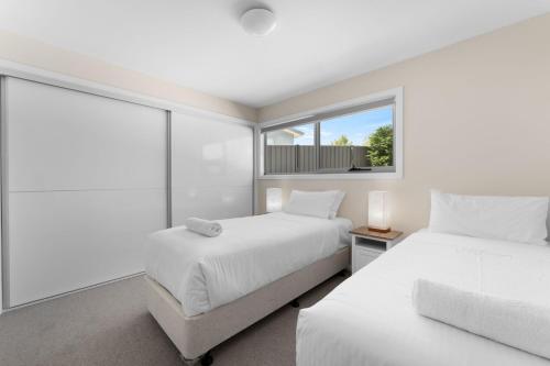 a white bedroom with two beds and a window at T Bar on Twynam in Jindabyne
