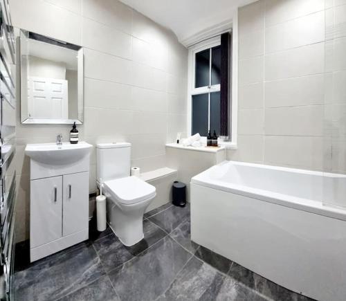 a white bathroom with a tub and a toilet and a sink at Luxury, Interior-Designed, Spacious Home in Harrogate