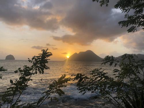 una puesta de sol sobre el agua con montañas en el fondo en Diamantchery - Vue mer avec Deck privatif en Le Diamant