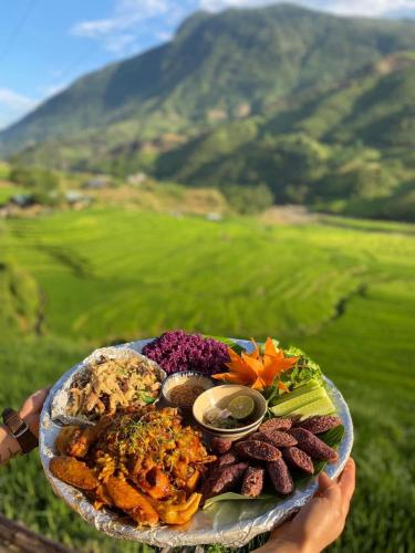 a person holding a plate of food with mountains in the background at En Hotel Sapa in Sa Pa