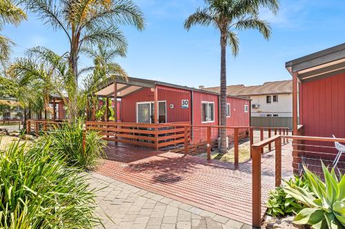 a red house with a deck and palm trees at Tween Waters Merimbula in Merimbula