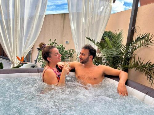 un homme et une femme assis dans un bain à remous avec un verre de vin dans l'établissement B&B Roomantic & Piscina Idromassaggio, à Cefalù