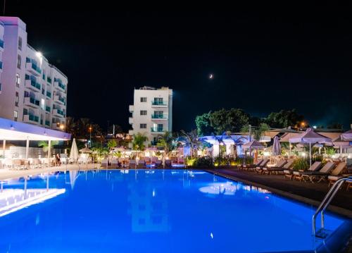 a large swimming pool with blue water at night at Kapetanios Bay Hotel Protaras in Protaras