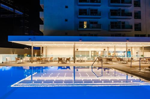 an outdoor pool with tables and chairs at night at Kapetanios Bay Hotel Protaras in Protaras