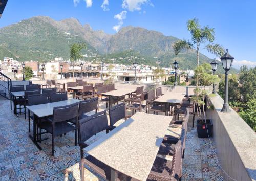 a restaurant with tables and benches with mountains in the background at Hotel The Grand Dewan in Katra