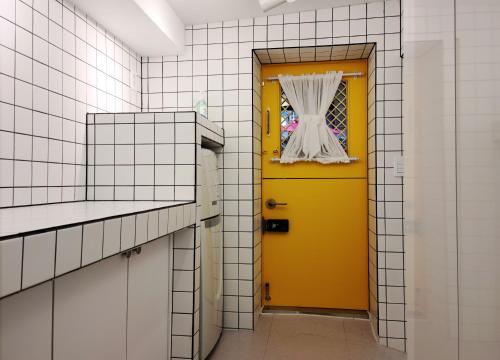 a yellow door in a bathroom with white tiles at Batwo Stay - For foreigners only in Seoul
