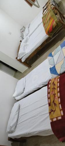 two beds in a room with white sheets and pillows at Raagabynature home stay in Gendehalli