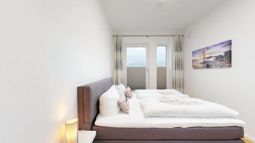 a bedroom with a bed with white sheets and a window at DünenResort in Binz, strandnahe und moderne FeWos mit Balkon, teilweise mit Meerblick, in Binz