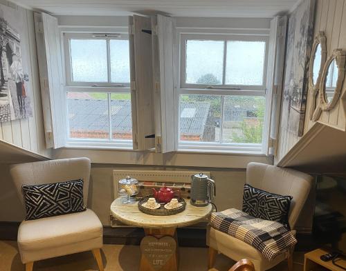 ein Wohnzimmer mit 2 Stühlen, einem Tisch und 2 Fenstern in der Unterkunft The Foulsyke Licensed Bed and Breakfast Scalby Scarborough in Scarborough