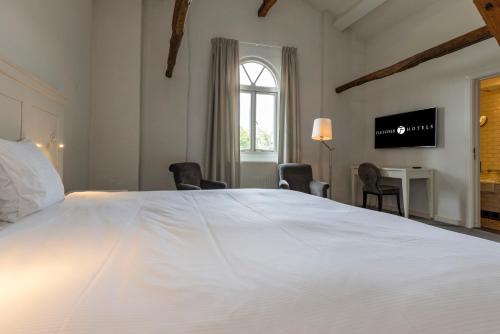 a bedroom with a large white bed and a desk at Fletcher Hotel Château De Raay in Baarlo