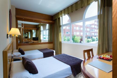 a room with two beds and a table and a window at VP Jardín de Tres Cantos in Tres Cantos