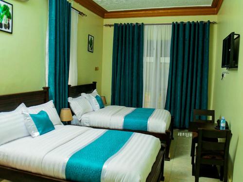 two beds in a hotel room with blue curtains at Bwiranda Hotel in Kasese