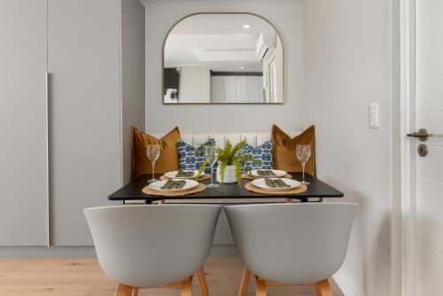 uma mesa de jantar com 2 cadeiras brancas e um espelho em 7 on Bantry Apartments na Cidade do Cabo