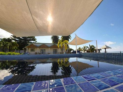 a swimming pool with an umbrella and a house at Le Uaina Beach Resort in Falepuna