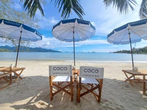 ein paar Stühle und Sonnenschirme am Strand in der Unterkunft Coconut Beach Resort, Koh Chang in Ko Chang