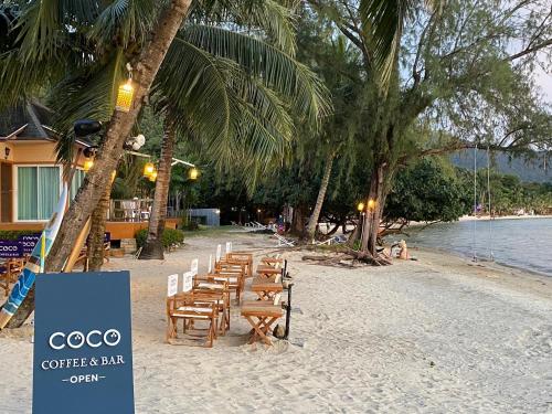 een rij houten tafels en stoelen op een strand bij Coconut Beach Resort, Koh Chang in Ko Chang