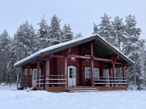 una pequeña cabaña de madera en la nieve con árboles en Kenttäniemi Cottages en Sonka