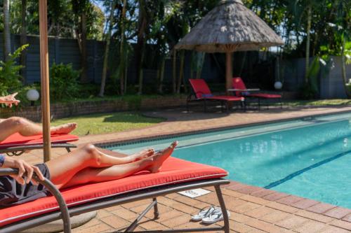 a woman laying on a chaise lounge next to a swimming pool at Indaba Lodge Hotel Richards Bay in Richards Bay