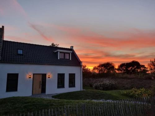a white house with a sunset in the background at Coastal Cottages huisje Bries in Ouddorp