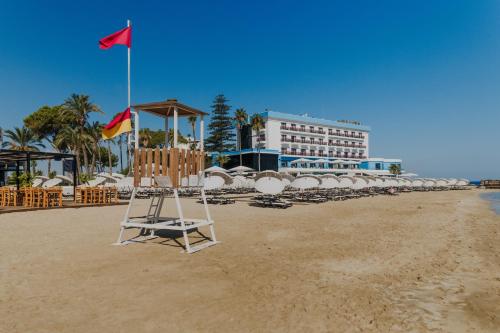 a beach with a flag and chairs and a hotel at Arkin Palm Beach Hotel in Mağusa