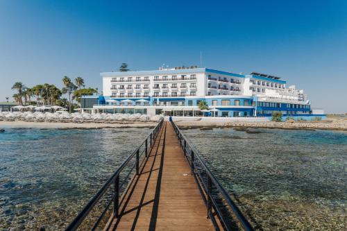 a large building on the beach with a wooden bridge at Arkin Palm Beach Hotel in Famagusta