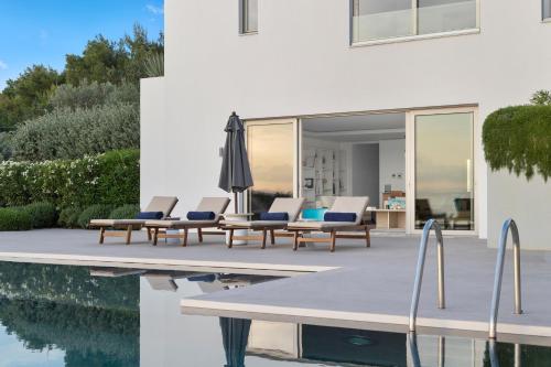 a group of chairs and an umbrella next to a pool at Villa Artemis - New Magnificent Beachfront Villa with Infinity Pool! in Kranidi