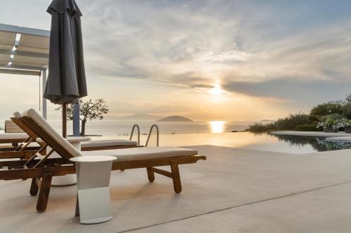 a patio with chairs and an umbrella and the ocean at Villa Artemis - New Magnificent Beachfront Villa with Infinity Pool! in Kranidi