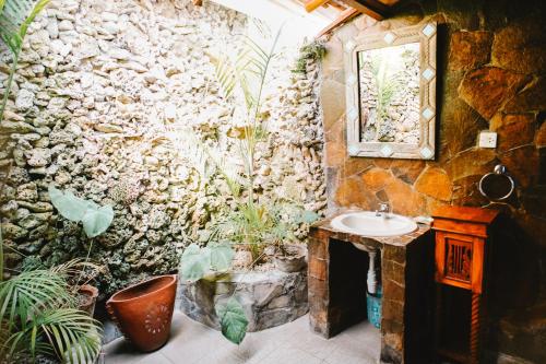 a bathroom with a stone wall with a sink and plants at Temple Cafe & Cottages in Candidasa