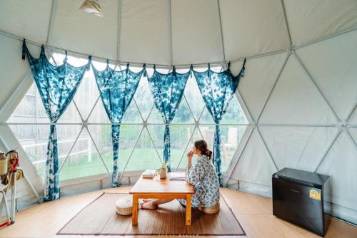 eine Frau, die an einem Tisch in einem Zimmer mit Fenstern sitzt in der Unterkunft Ikigawa Home in Ban Pha Khap