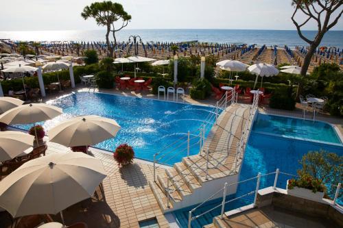 a swimming pool with umbrellas and chairs and the ocean at Ruhl Beach Hotel & Suites in Lido di Jesolo