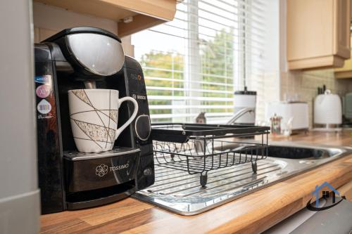 a toaster sitting on a kitchen counter with two cups at Garfield House, 3 bed house, sleeps 7, Nr Rushden Lakes, allocated parking, corporates welcome in Wellingborough