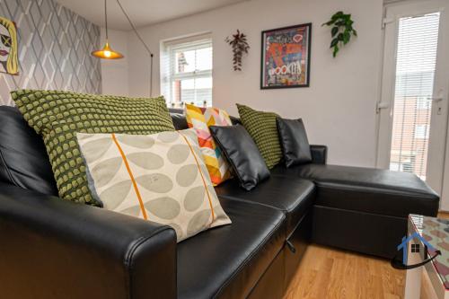 Un sofá de cuero negro con almohadas coloridas. en Garfield House, allocated parking, free wi-fi, pets, corporates welcome en Wellingborough