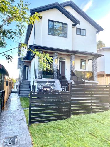 a white house with a fence in front of it at Modern and New house near PNE with Big Garden and Free Parking in Vancouver