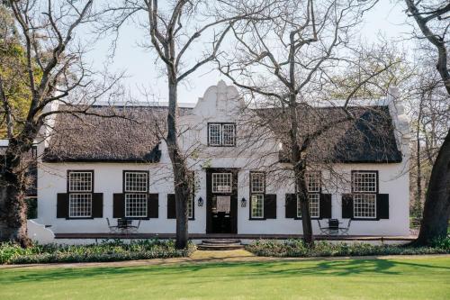 ein weißes Haus mit schwarzen Fenstern und Bäumen in der Unterkunft Blaauwklippen Manor by NEWMARK in Stellenbosch