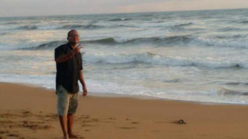 un hombre parado en la playa cerca del océano en Ora en Kalutara