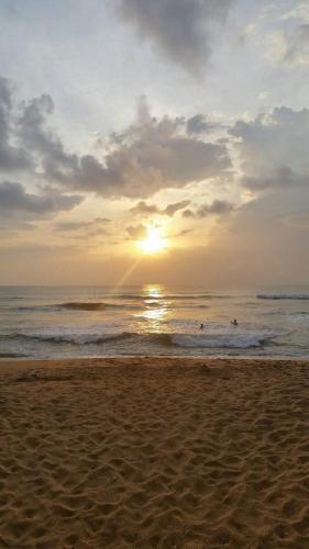 a sunset on the beach with people in the water at Ora in Kalutara