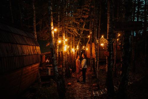 two people standing in a forest at night with lights at Jurty z widokiem, prywatna balia- DZIKOLAS GLAMPING in Krasnobród