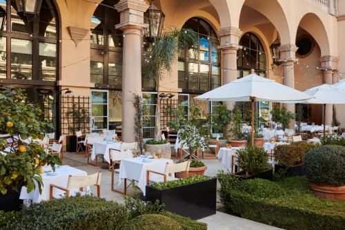 um restaurante com mesas e guarda-sóis em frente a um edifício em The Maybourne Beverly Hills em Los Angeles