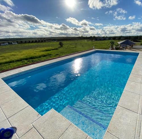 a large blue swimming pool with a field in the background at Quinta Da Amoreira in Ferreira do Alentejo