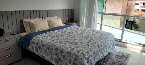 a bed with a blue and white comforter and a window at Pousada Rota do Sol Bombinhas suítes com café e sem limpeza diaria in Bombinhas